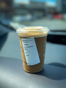 Portrait shot of a cup of iced coffee in focus on a dashboard with a blurred background