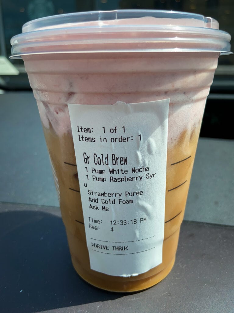 Iced coffee drink with pink foam in a cup on a dashboard 