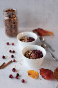 Side shot of two bowls of hot cereal with a jar of pecans nearby