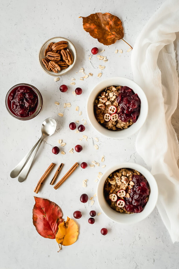 Top down view of bowls of hot cereal surrounded by cranberries and cinnamon sticks