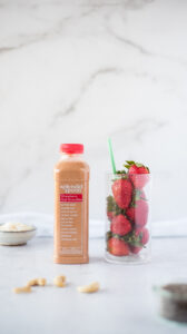 Bottle of fruit smoothie next to a glass full of strawberries