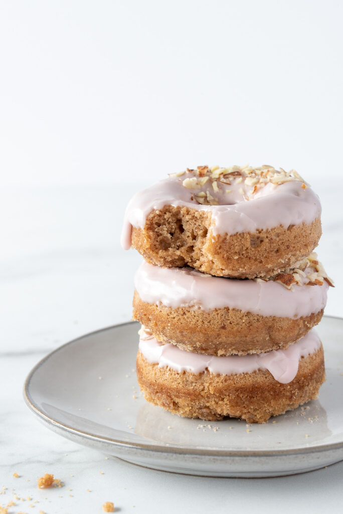 Three donuts with pink frosting stacked on a plate