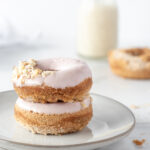 Two donuts stacked on a plate with a small pitcher of milk