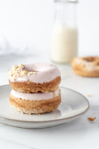 Two donuts stacked on a plate with a small pitcher of milk