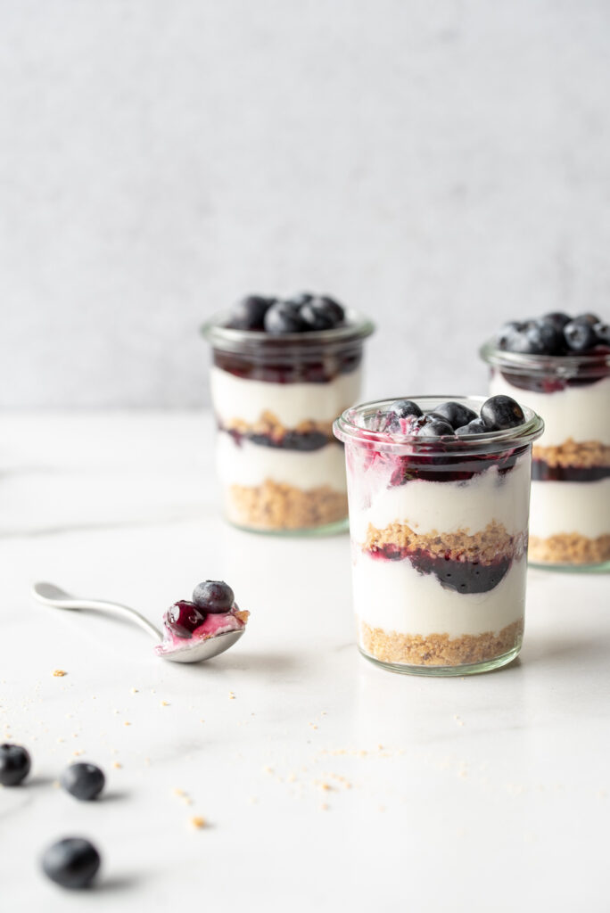 Three jars of blueberry cheesecake and a spoon with a bite out of one jar