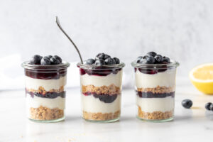 Three jars of blueberry cheesecake with a lemon and blueberries
