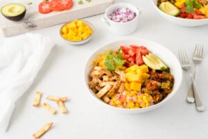 Bowl of taco ingredients surrounded by small bowls of mango, tomato, onion