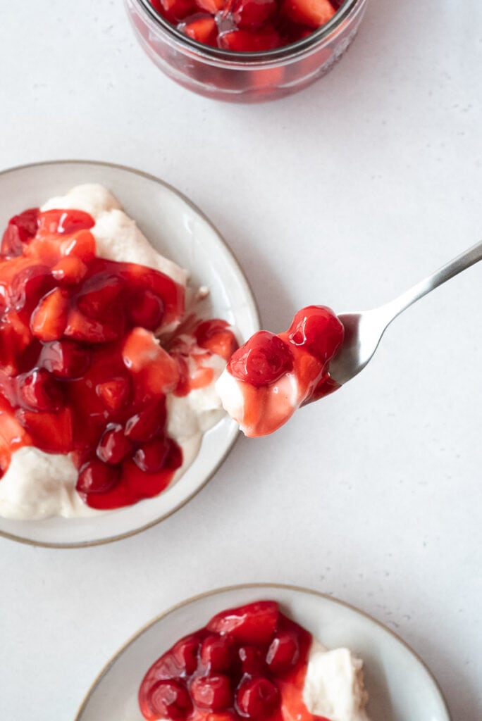 Fork lifting one bite of meringue dessert with cherries over plate