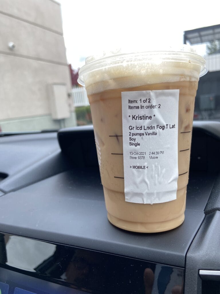 Grande iced Starbucks drink sitting on the dashboard of a car