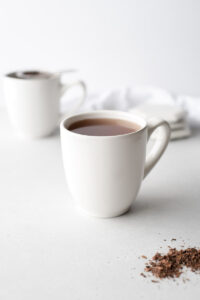 Two white cups of cacao husk tea in front of a napkin