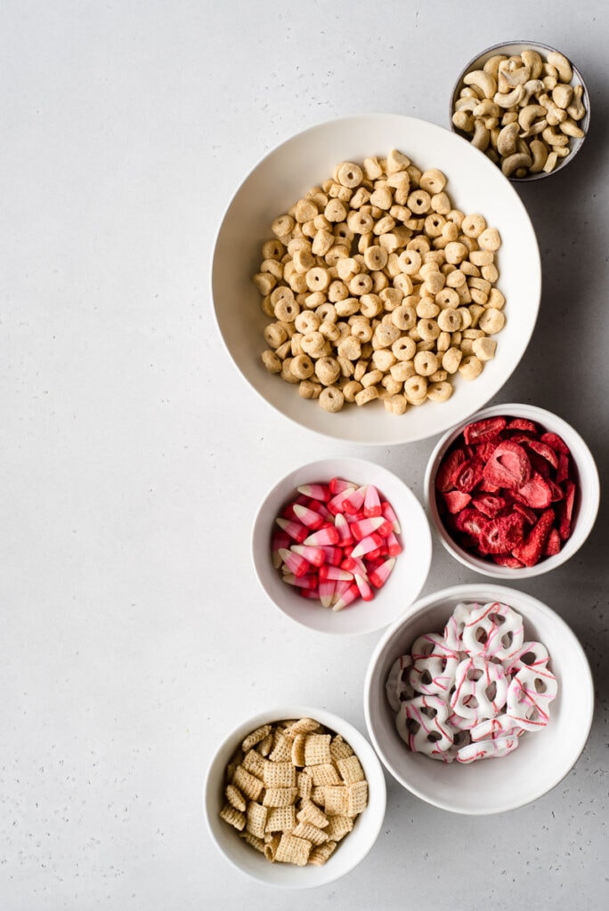 Top down view of 6 bowls filled with cereal, pretzels, dried strawberries and candy corn