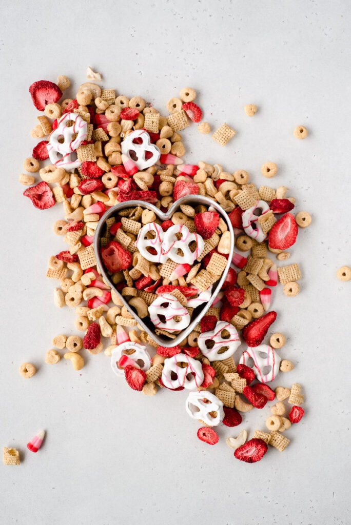 Top down view of heart shaped pan full of Valentine snack mix surrounded by more snack mix