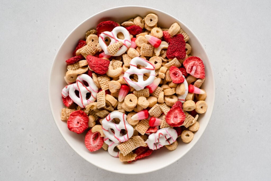 Top down view of white bowl full of red and white snack mix