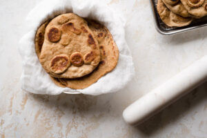 Stack of naan in a bowl next to rolling pin