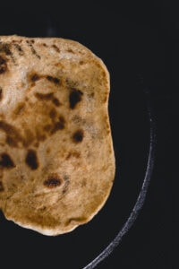 Naan bread being cooked on a cast iron griddle
