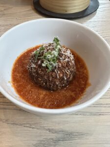 White bowl with a cooked rice ball sitting on a bed of tomato sauce