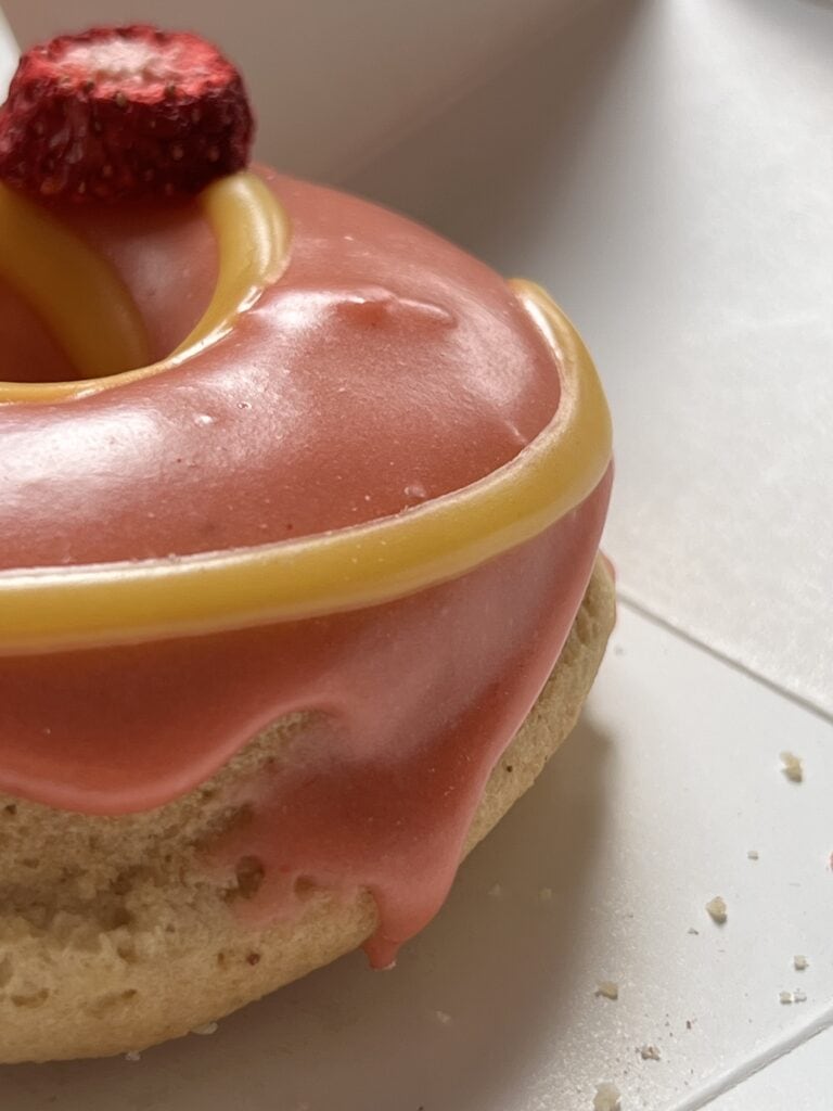 Close up of a donut with pink frosting and yellow stripes