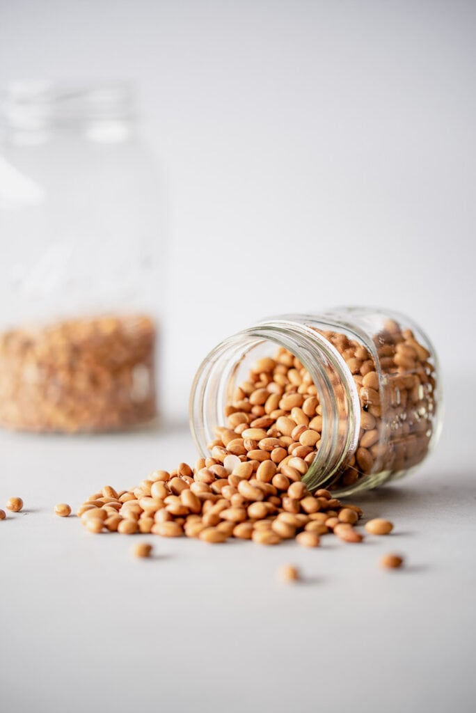 Two glass jars full of rust-colored beans, and some are spilling out onto a white surface