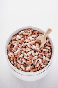 Large white bowl of brown and white speckled beans with a small wooden scoop