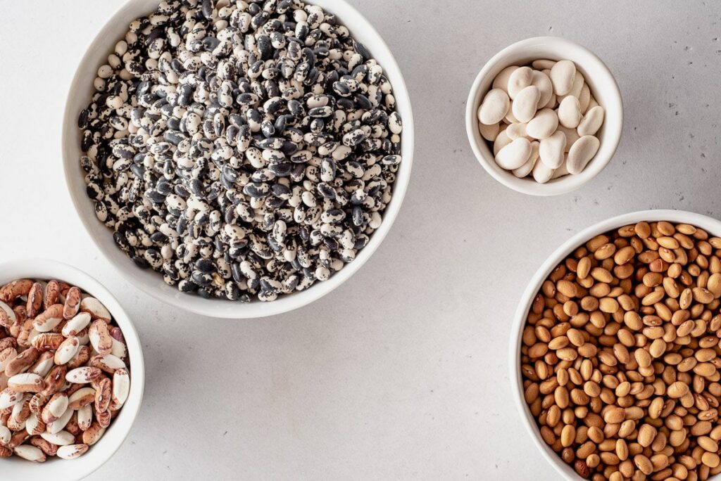 Four bowls of differing sizes viewed from the top, all filled with different colored dry beans