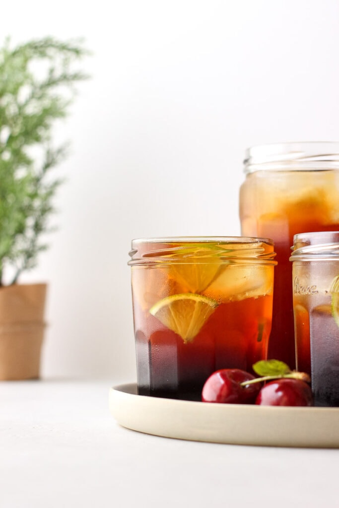 Three glasses of cherry shrub garnished with lime next to some fresh cherries