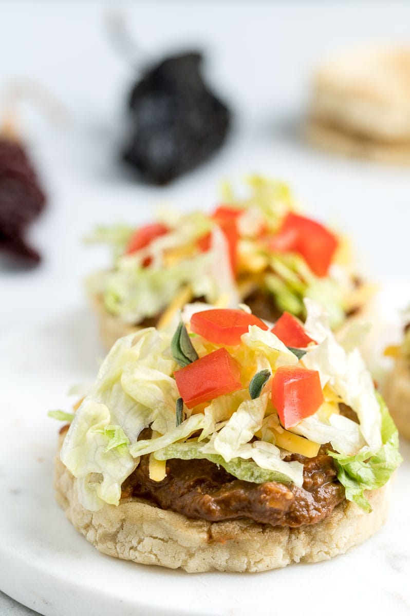 Two masa shells topped with mole, lettuce and tomato