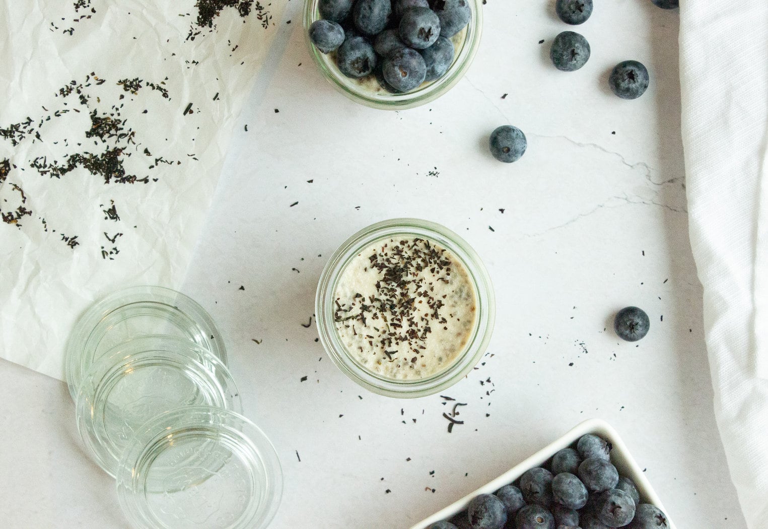 Top down view of jar of chia pudding, napkin, blueberries, and scattered tea leaves