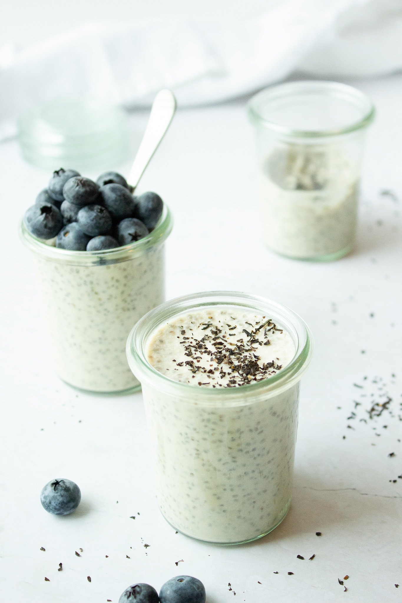 Side view of 3 jars of chia pudding with blueberries on a white background