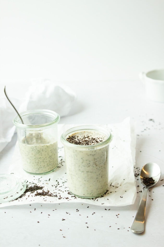 Two small jars of chia pudding and a spoon on a white background