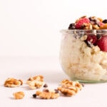 Glass bowl filled with rice pudding and fruit next to some walnuts