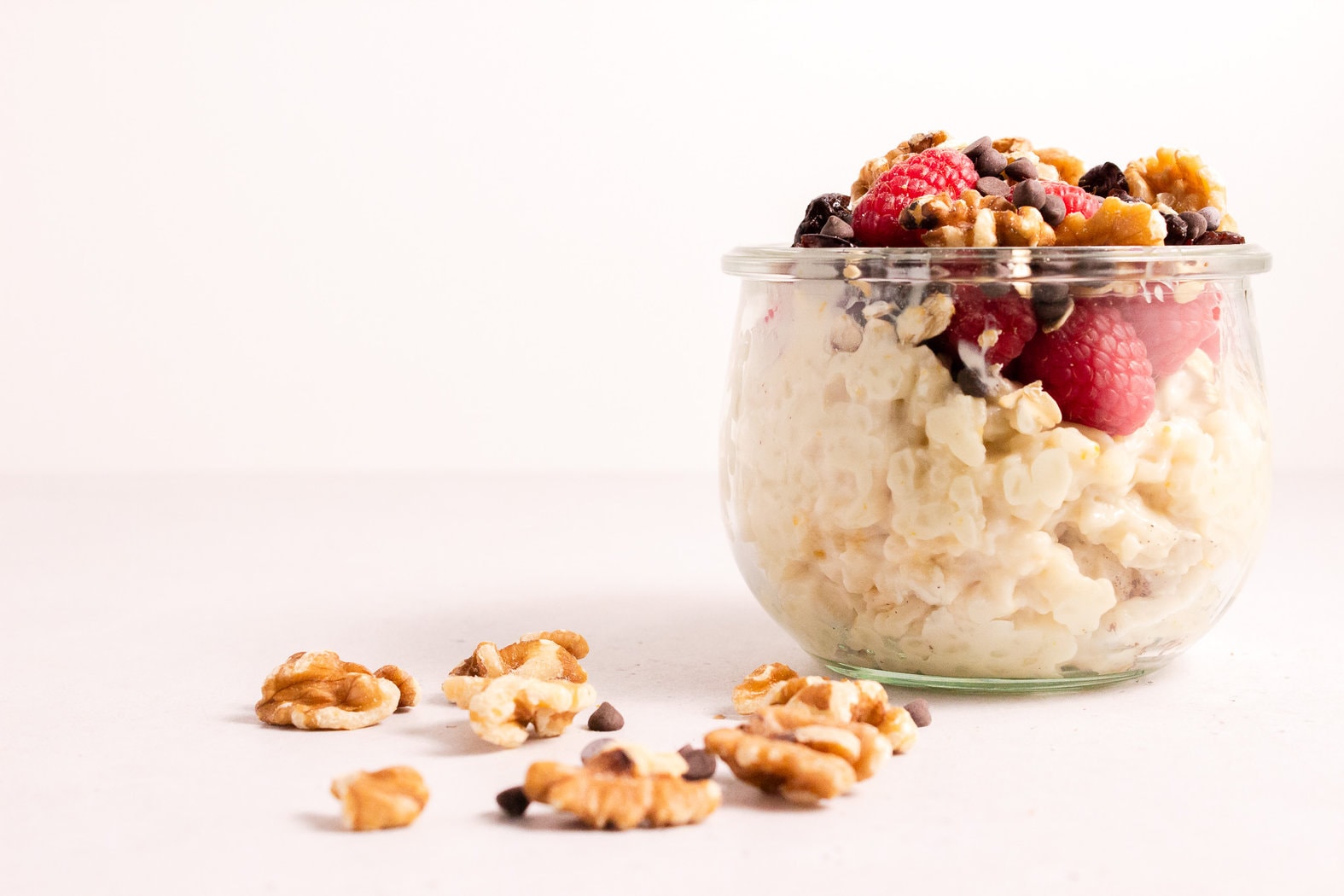 Glass bowl filled with rice pudding and fruit next to some walnuts