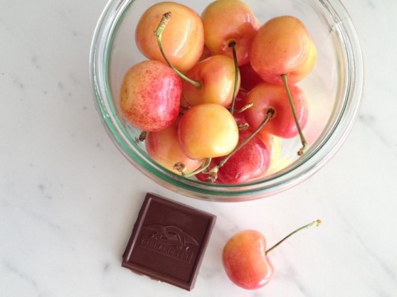 small jar filled with cherries next to 1 square of dark chocolate