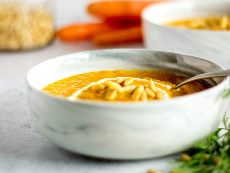 Bowl of carrot soup, pine nuts, bunch of carrots