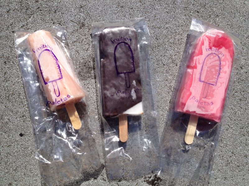 Top down view of 3 popsicles in wrappers on concrete