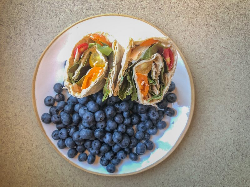Wrap sandwich standing up on a plate surrounded by blueberries